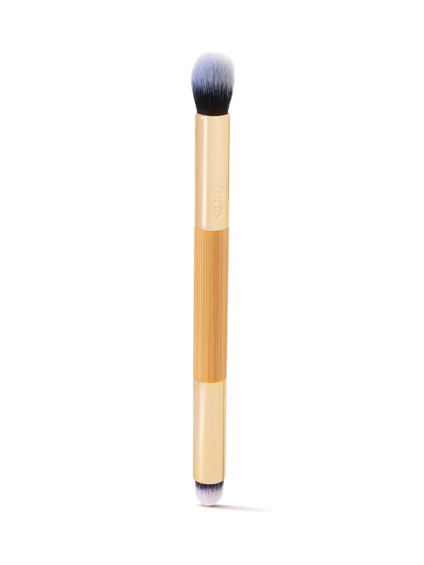 A dual-ended makeup brush with tan handles and soft bristles, one end rounded and the other pointed, is oriented vertically on a white background. The handle displays tarte.