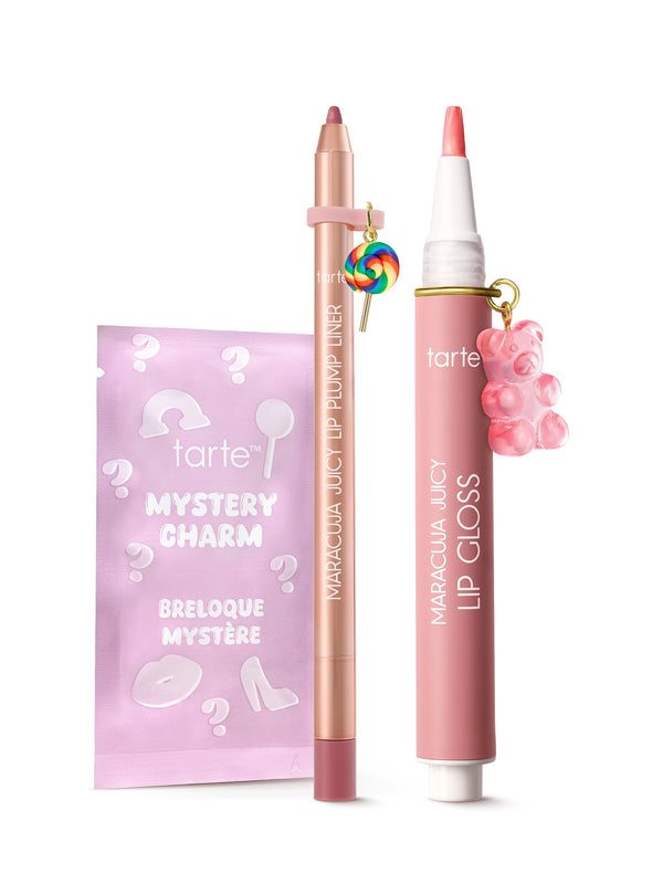 A pink maracuja juicy lip gloss pen and matching lip liner stand upright, each adorned with a small charm, beside a pastel purple mystery charm sachet on a white background.
Text: tarte™ MYSTERY CHARM BRELOQUE MYSTÈRE; tarte; MARACUJÁ JUICY LIP PLUMP LINER; MARACUJÁ JUICY LIP GLOSS