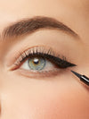 Close-up of an eye with eyeliner being applied, with a makeup pencil visible.