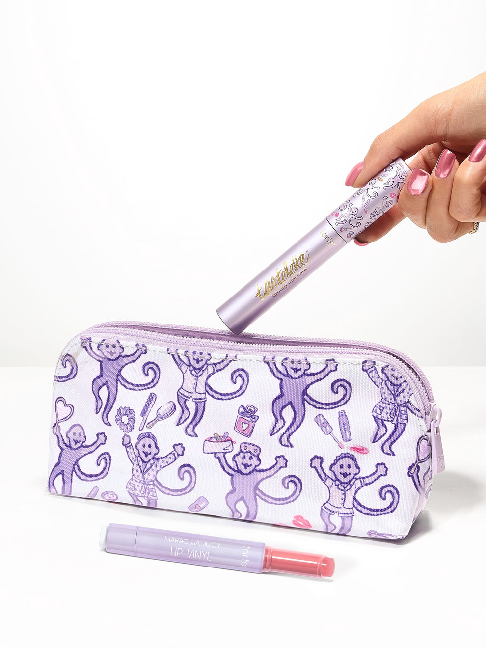 woman holding a tarte cosmetics x roller rabbit collaboration makeup bag, maracuja juicy lip vinyl, and tartelette tubing mascara against a white background