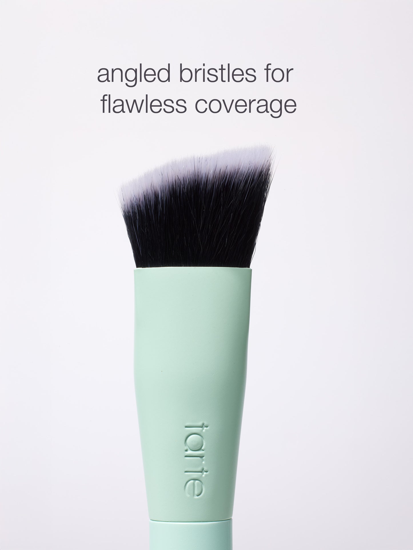 A mint green Tarte Cosmetics brush with angled bristles is showcased, designed for flawless coverage. The background is plain white. Text: angled bristles for flawless coverage.