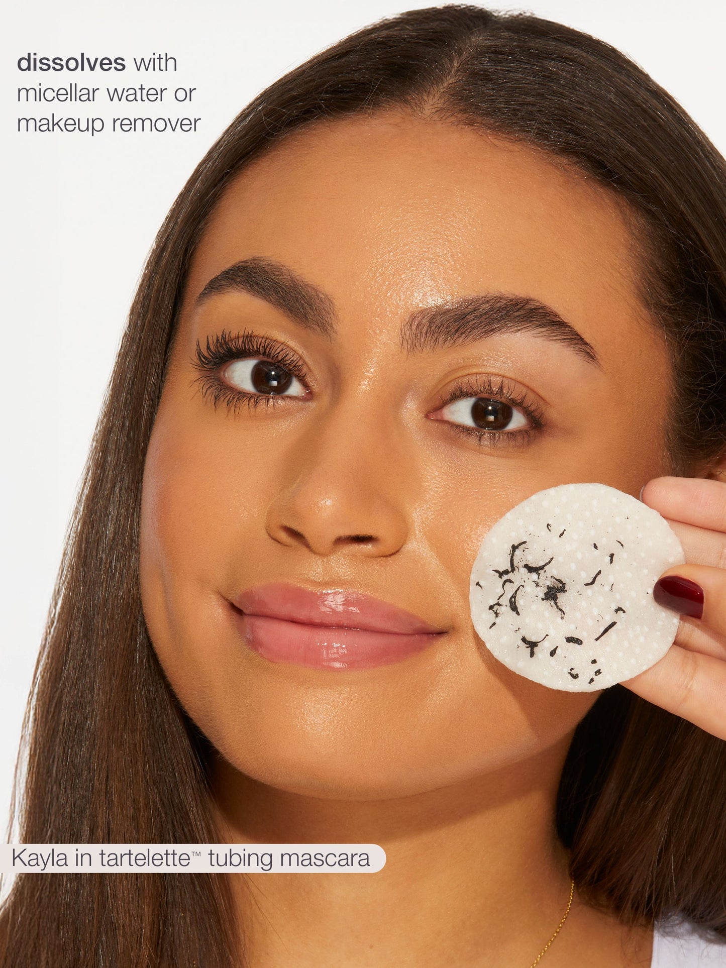 Woman holding a white round makeup pad with black specks, against a neutral background.