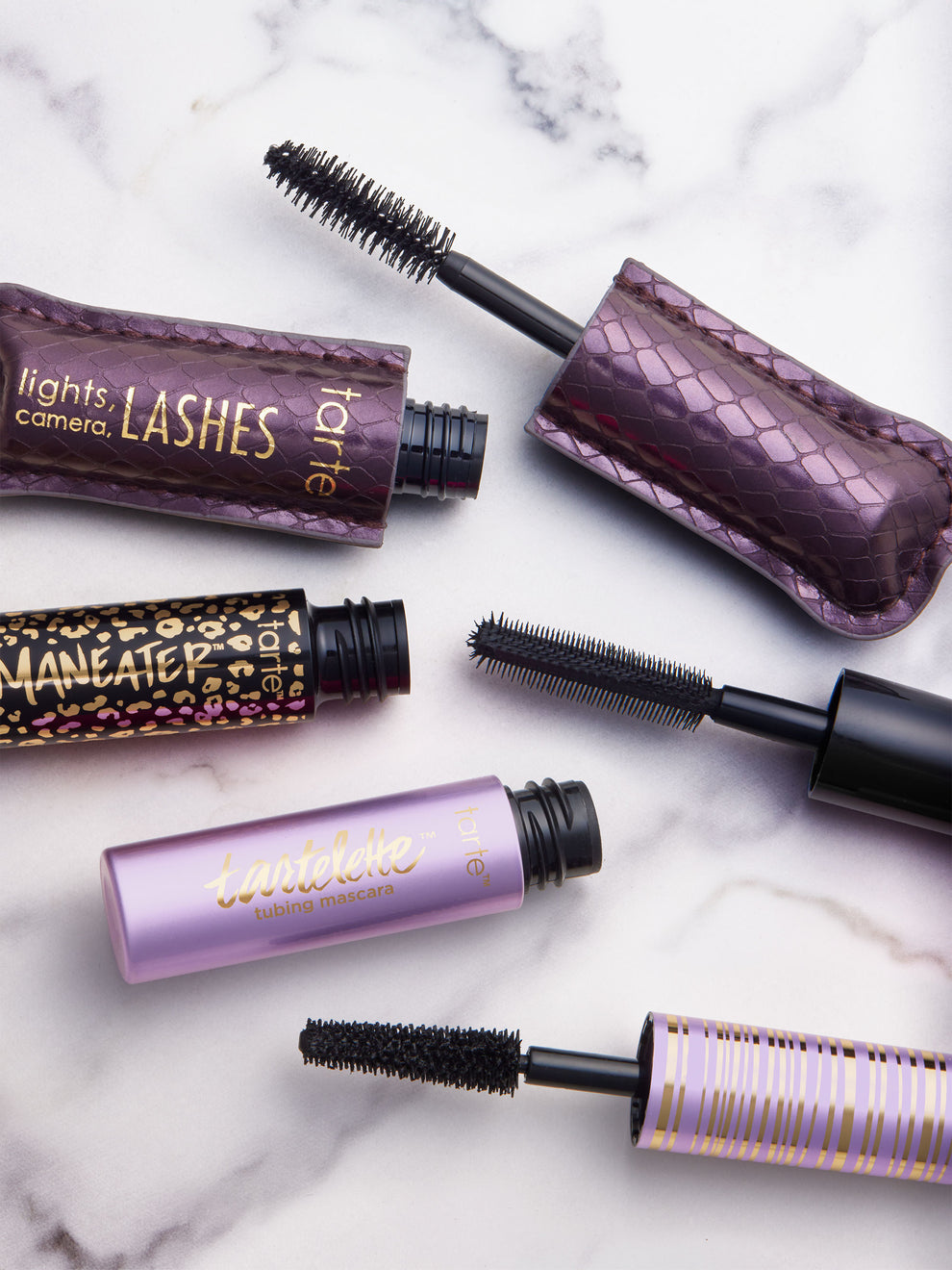 Collection of mascara tubes with purple and black packaging on a marble surface