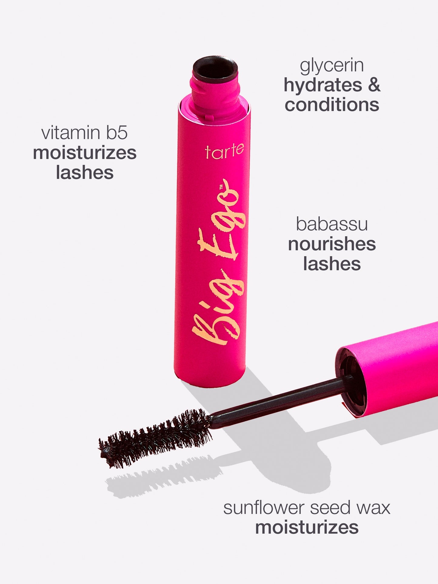 A pink tube of Tarte Cosmetics mascara labeled Big Ego with an attached brush is displayed against a white background. Text highlights ingredients: vitamin b5 moisturizes lashes, glycerin hydrates and conditions, babassu nourishes lashes, sunflower seed wax moisturizes.