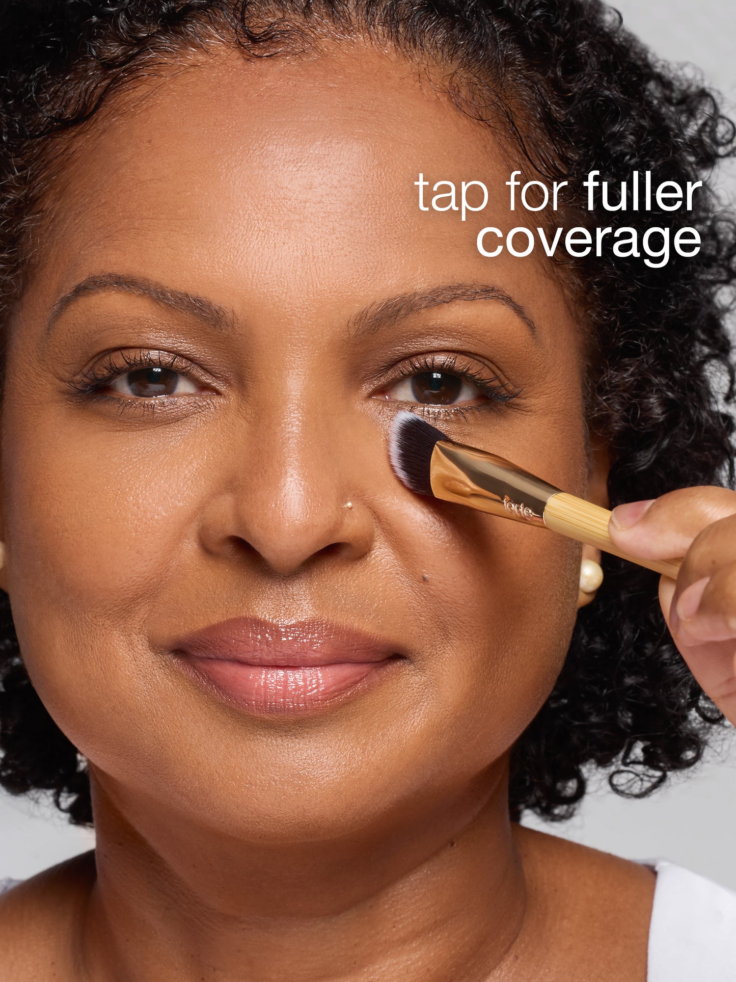 Woman applying makeup with a brush, text 'tap for fuller coverage' displayed.