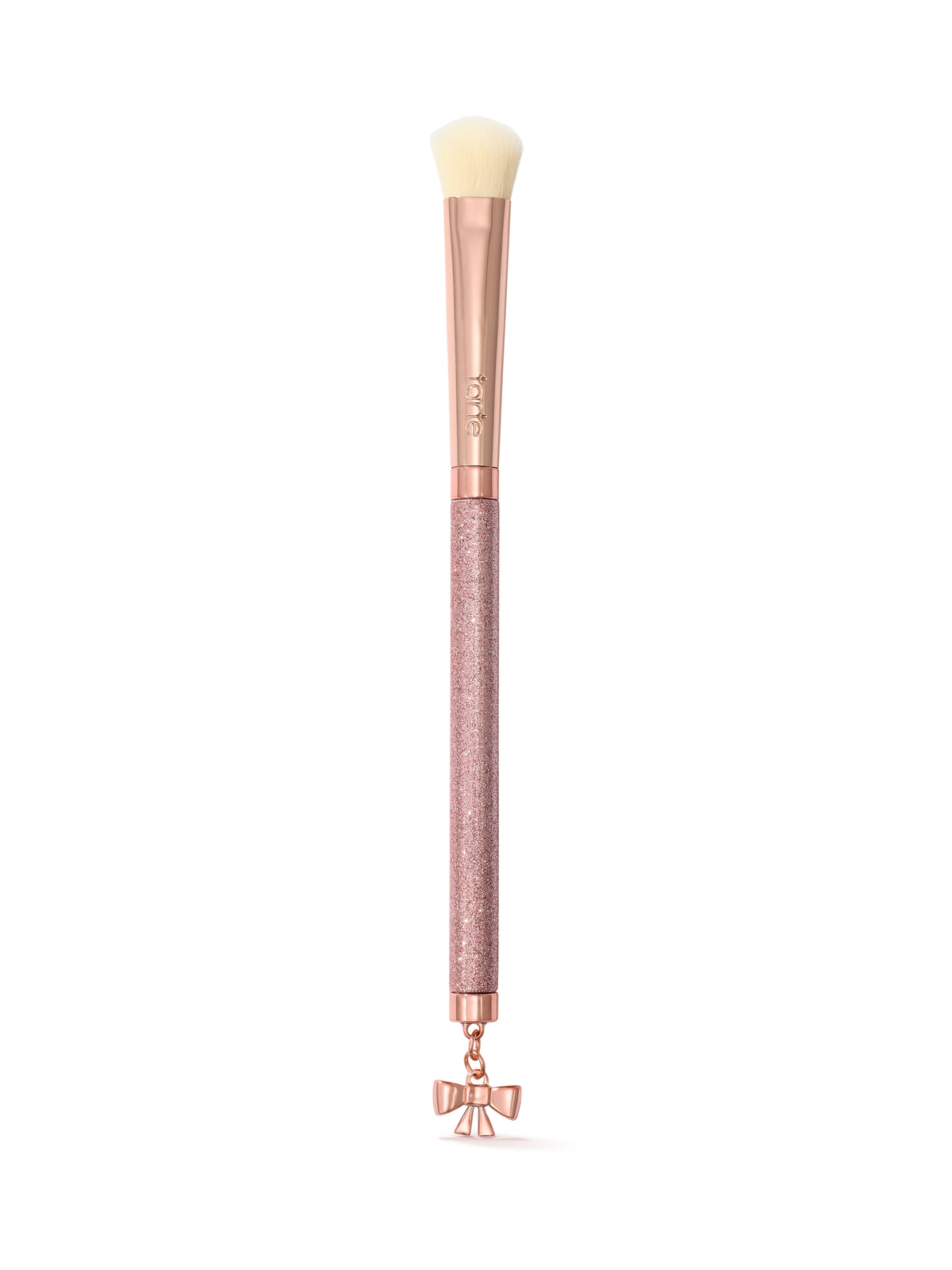 A makeup brush with a rose gold handle, a textured pink glitter grip, and a dangling bow charm at the bottom, shown on a clean white background.