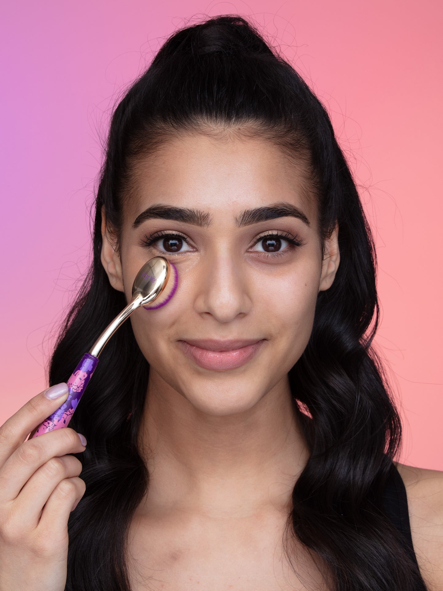 Woman applying cream to her face with a brush against a pink gradient background
