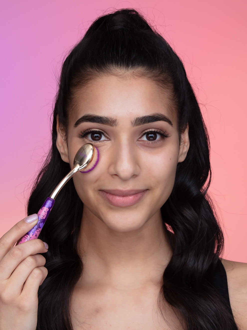 Woman applying cream to her face with a brush against a pink gradient background