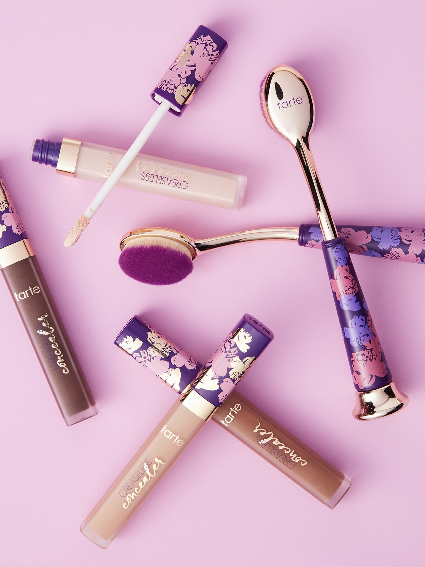 Makeup products including lip glosses and a brush on a pink background