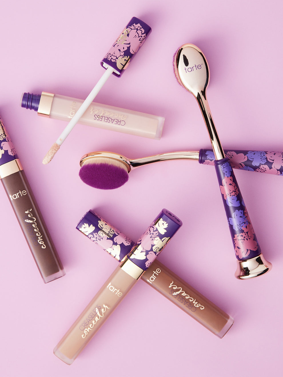 Makeup products including lip glosses and a brush on a pink background