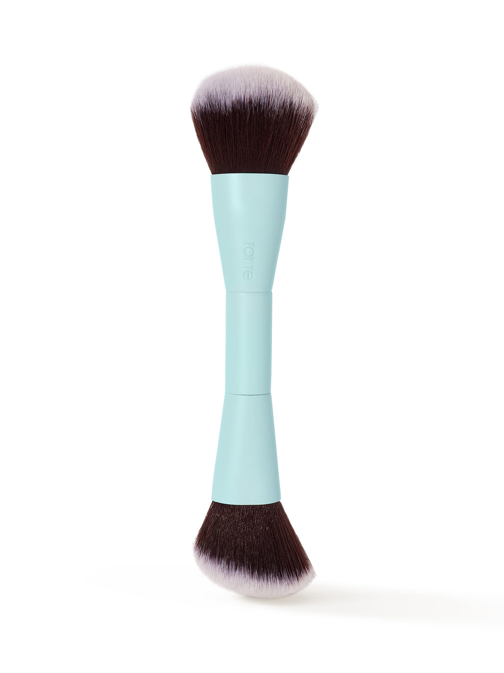A double-ended makeup brush with brown and white bristles stands upright. The handle is light blue and features the text tarte embossed on it, set against a plain white background.