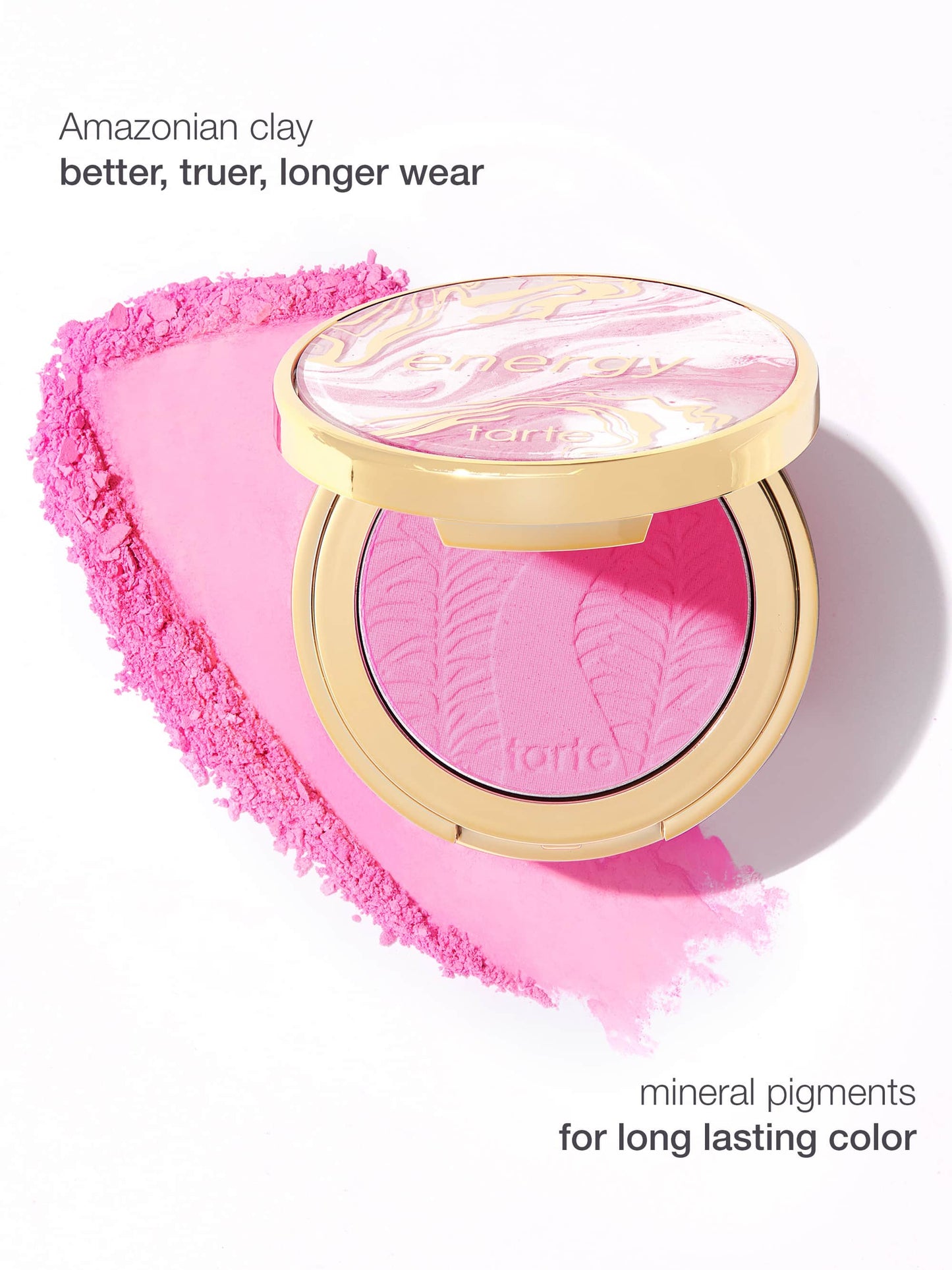 A round, open compact of Tarte Cosmetics blush rests on a bed of crushed pink powder. Text reads, Amazonian clay better, truer, longer wear and mineral pigments for long lasting color.