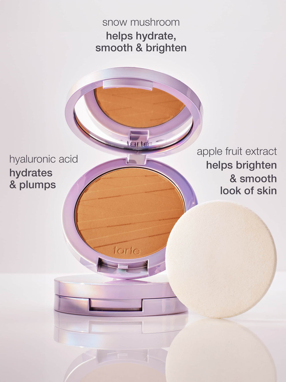 A Tarte Cosmetics powder compact is open, displaying its product alongside a white application sponge. Text highlights ingredients: snow mushroom helps hydrate, smooth & brighten, hyaluronic acid hydrates & plumps, apple fruit extract helps brighten & smooth look of skin. The background is a soft, neutral surface.