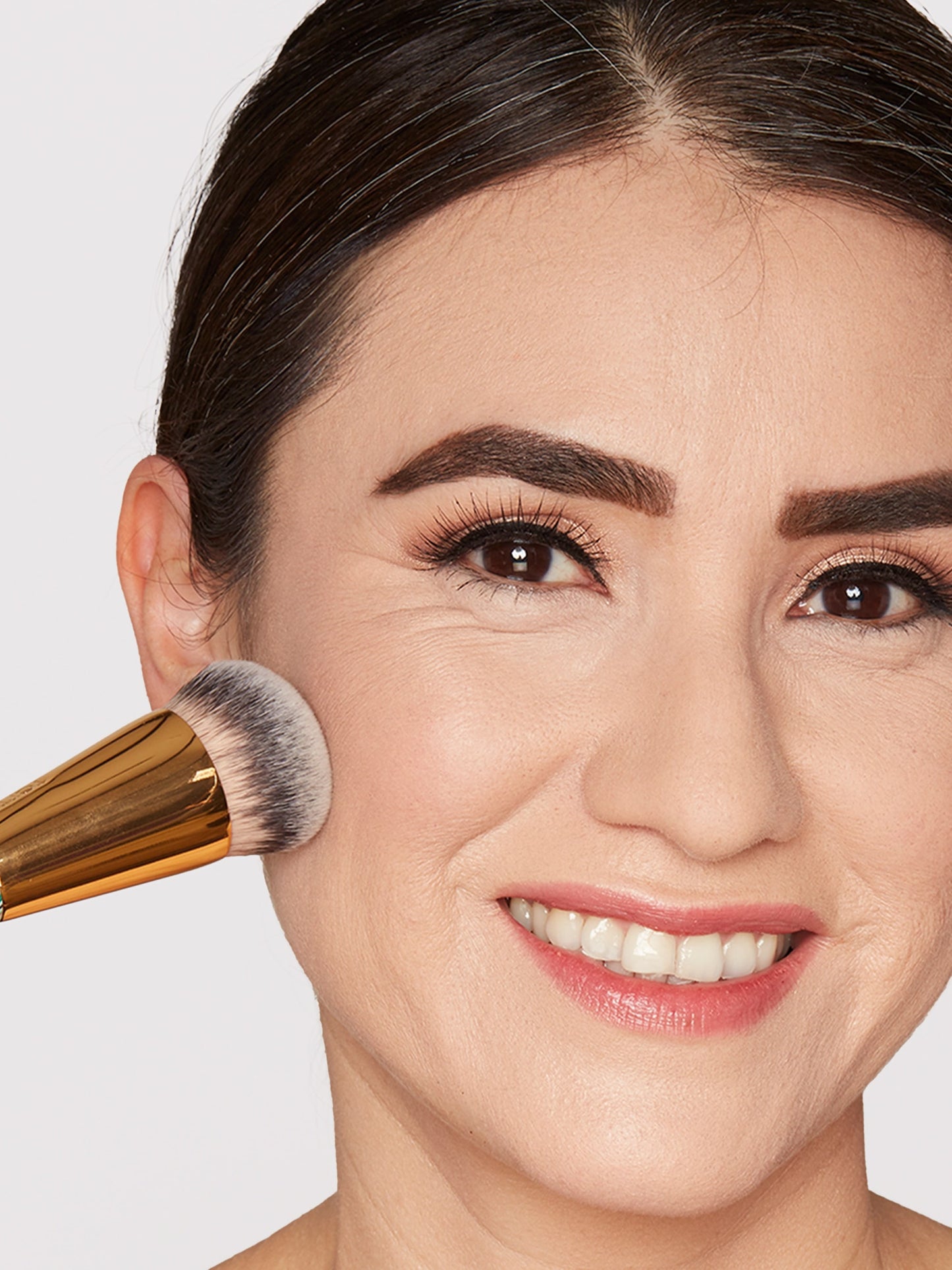 Woman with a makeup brush applying foundation to her face against a plain background