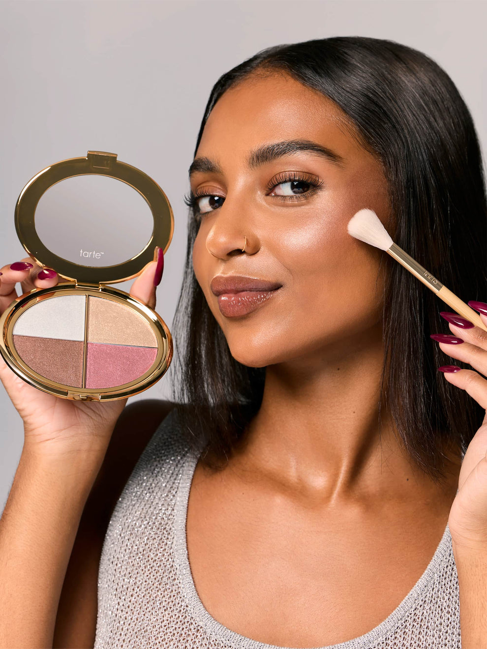 Woman applying makeup with a compact powder and brush, holding a compact mirror.