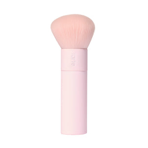 Um pincel de maquilhagem cor-de-rosa da marca Tarte Cosmetics, com cerdas macias e arredondadas e um cabo cor-de-rosa, sobre um fundo branco. 