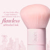 A light pink makeup brush with dense soft bristles and a pink handle, shown on a pink background with text  'flawless airbrushed look'