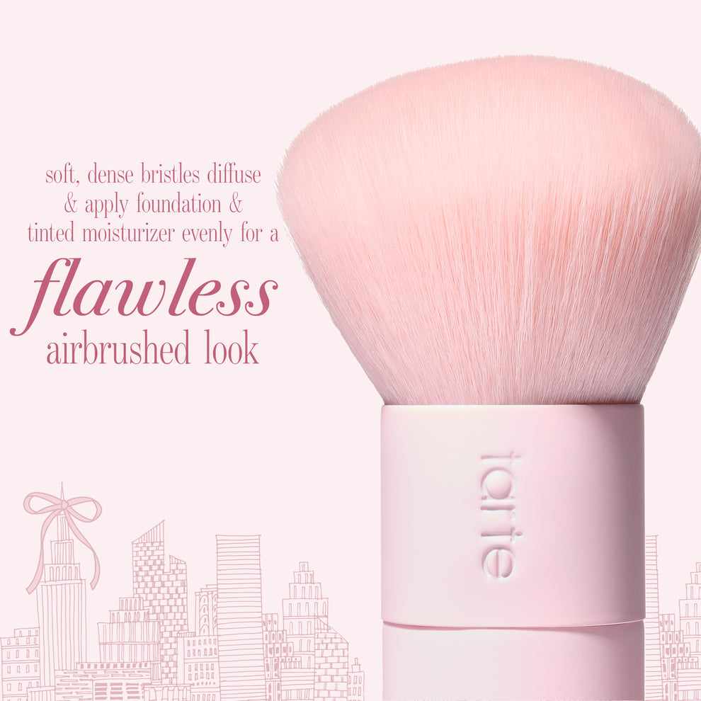 A light pink makeup brush with dense soft bristles and a pink handle, shown on a pink background with text  'flawless airbrushed look'