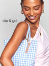 A person smiles while carrying a blue-checkered bag with a Tarte Cosmetics item clipped to it. The text clip & go! appears on the left.