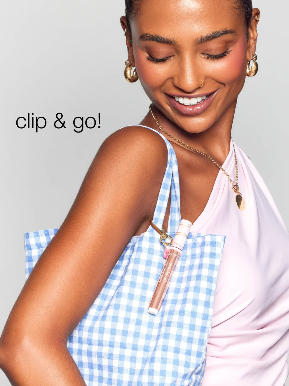 A person smiles while carrying a blue-checkered bag with a Tarte Cosmetics item clipped to it. The text clip & go! appears on the left.