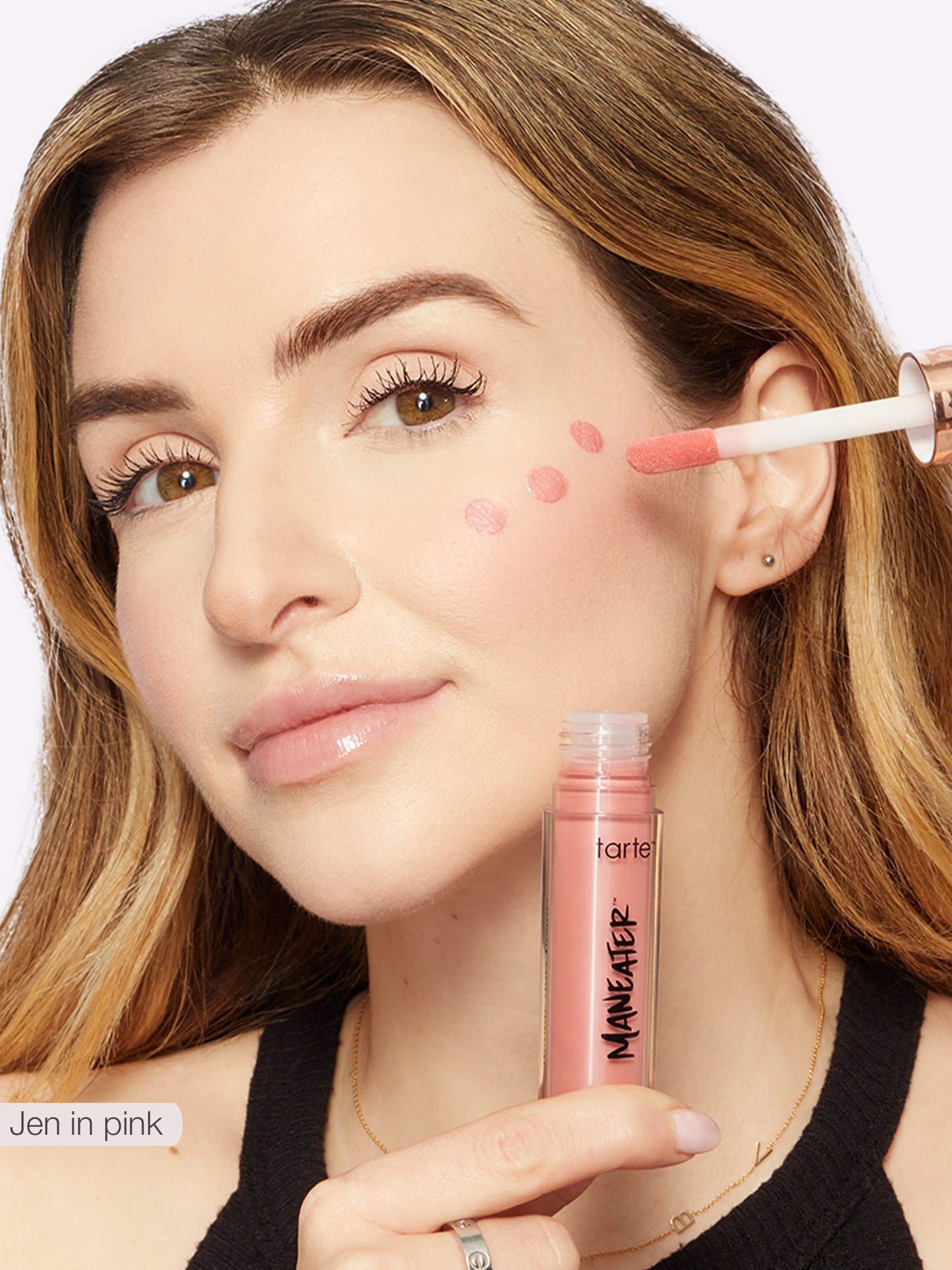 Woman applying makeup with a pink lip gloss applicator on a white background