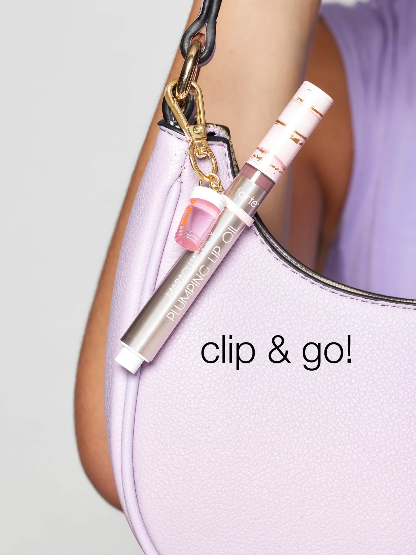 A tube of Tarte Cosmetics lip oil is clipped to a lavender handbag using a gold keyring. The text clip & go! is displayed on the bag.