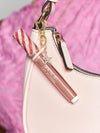 Lip gloss tube with a red and white glitter cap attached to a pink handbag by a gold clasp, featuring a small sparkling star charm. Background shows a pink fabric. Text: tarte MARACUJA JUICY LIP PLUMP.