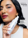 Woman holding a Tarte makeup spray with product features listed.