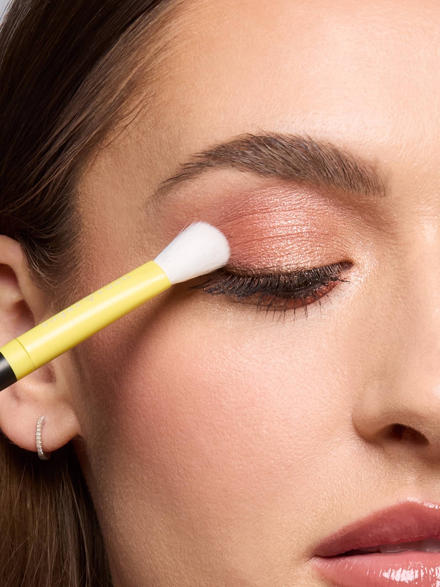 Close-up of a woman applying makeup with a brush to her eye.