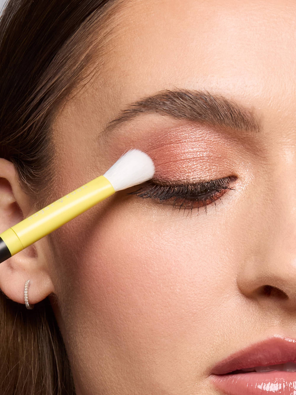 Close-up of a woman applying makeup with a brush to her eye.