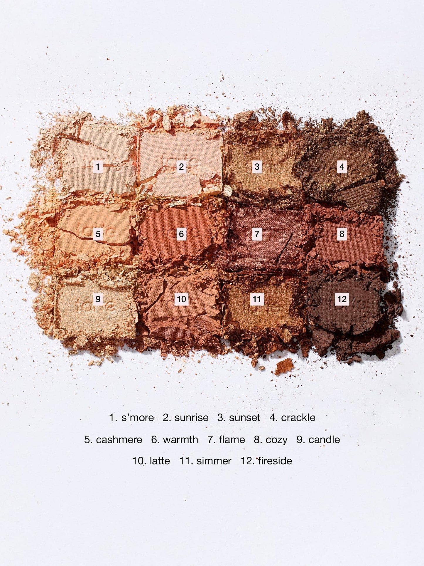 Crushed Tarte Cosmetics eyeshadow palette displays twelve labeled shades, including s’more, sunrise, sunset, crackle, cashmere, warmth, flame, cozy, candle, latte, simmer, and fireside, scattered on a white surface.