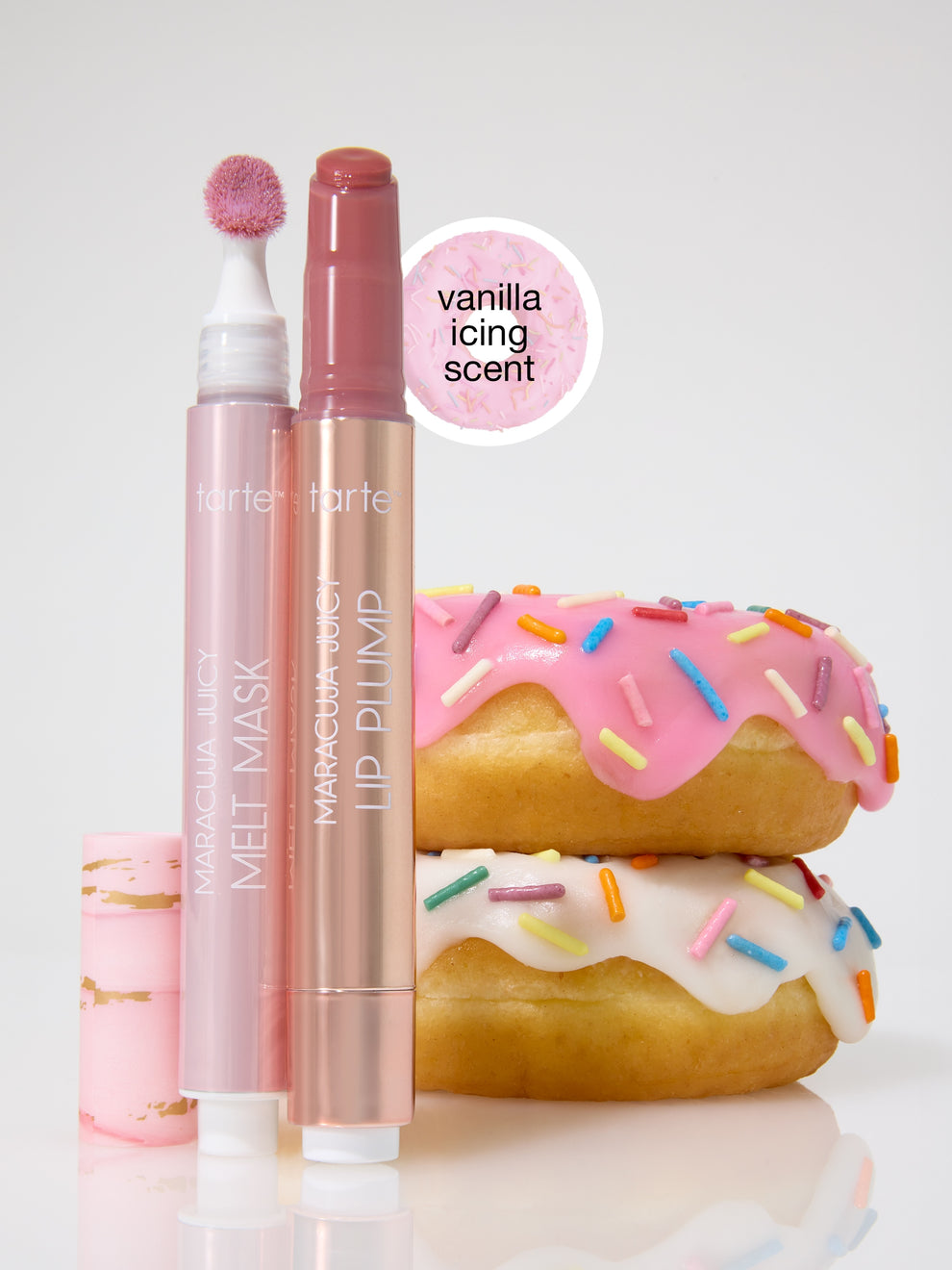 Two Tarte Cosmetics products, MARACUJA JUICY MELT MASK and LIP PLUMP, are positioned beside donuts with colorful sprinkles. A label reads vanilla icing scent on a pink circular background.