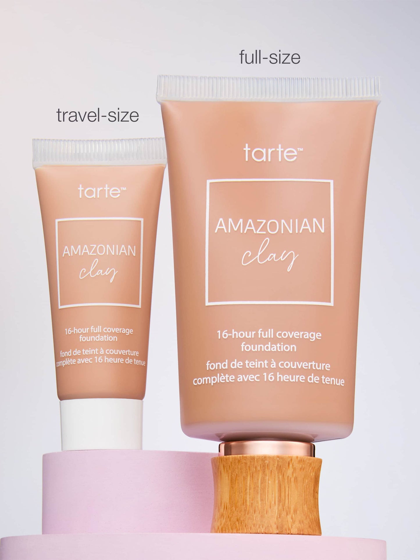 Two tubes of Tarte Cosmetics Amazonian Clay full coverage foundation, labeled travel-size and full-size, stand on a pastel platform. Both feature text: 16-hour full coverage foundation.