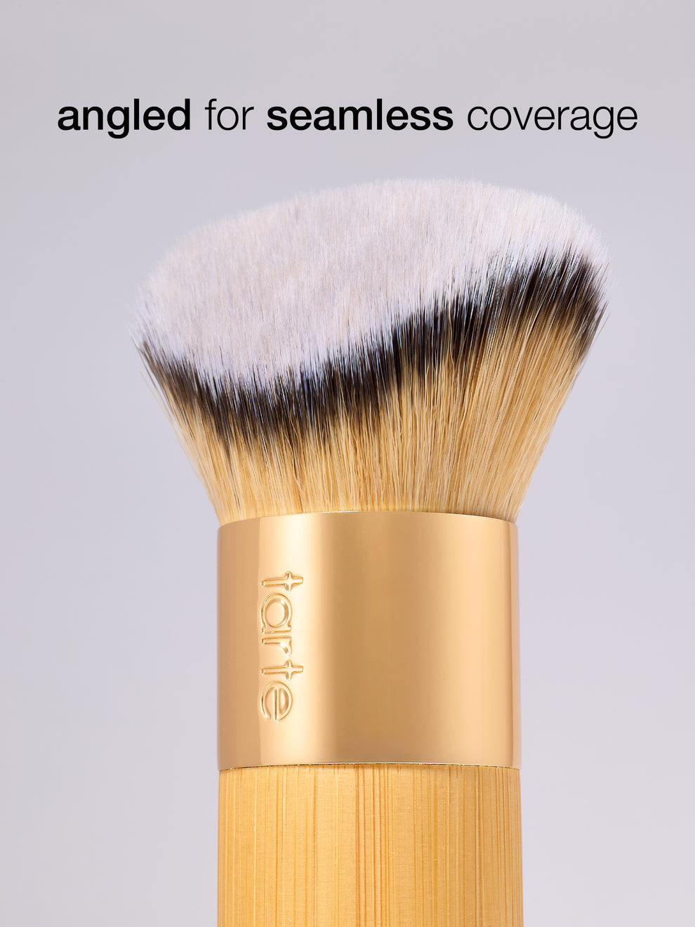 Makeup brush with gold handle and white bristles on a gray background, featuring the tarte logo.