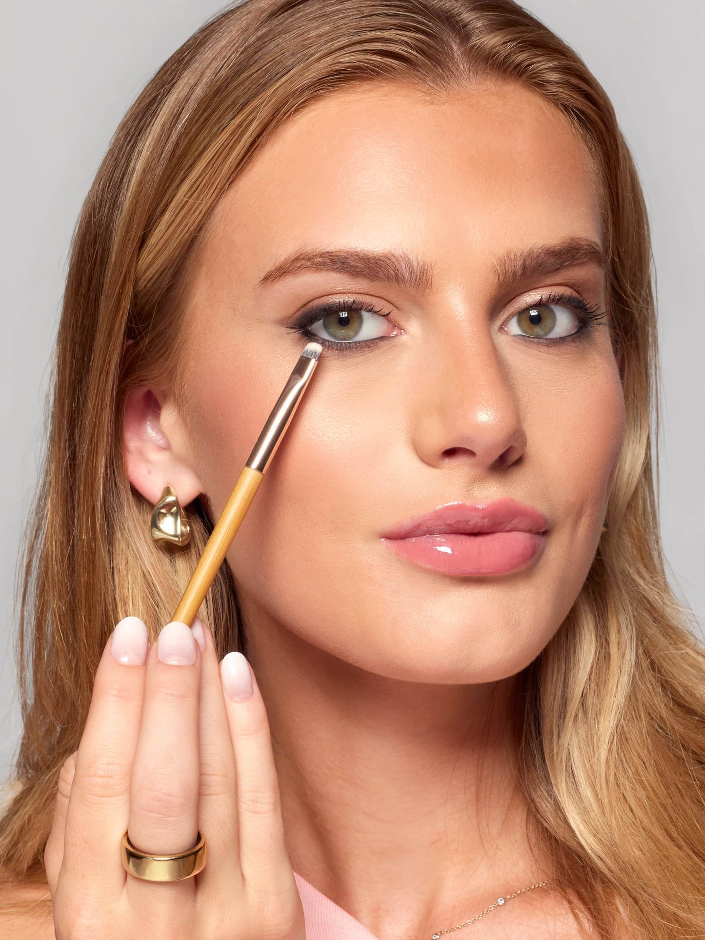 Woman applying makeup with a brush on a neutral background