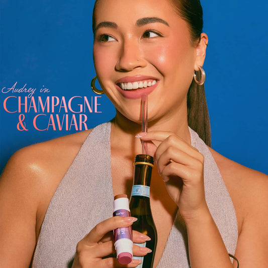 Woman holding a bottle with a straw against a blue background, with text 'Audrey in Champagne & Caviar'.