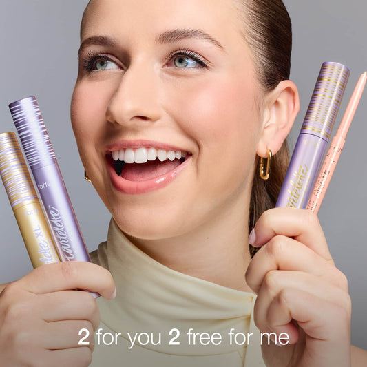 A smiling person holds two Tarte Cosmetics mascaras and a makeup product against a neutral background. Text at the bottom reads, 2 for you 2 free for me.