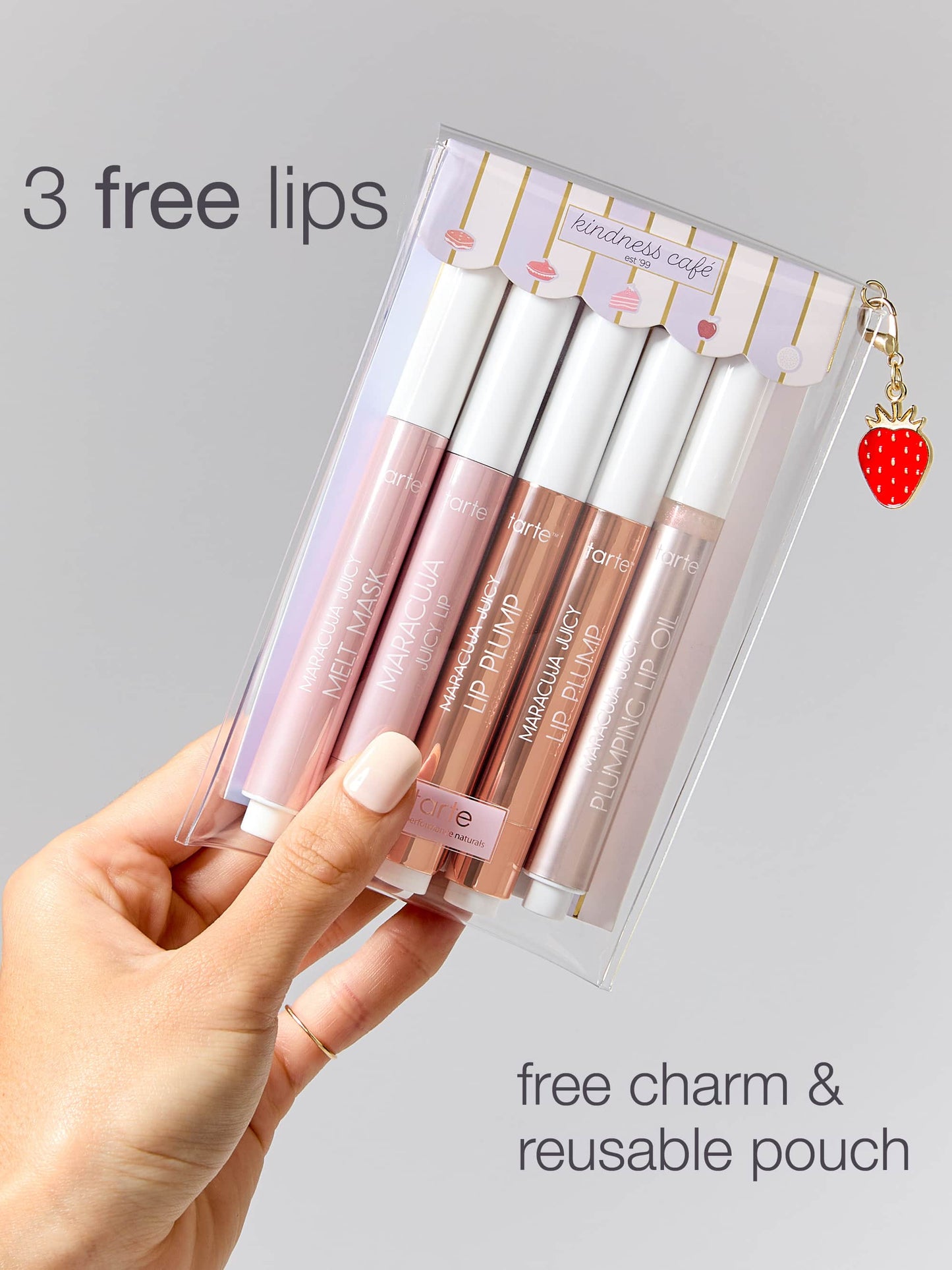 Set of lip glosses in a clear packaging with a charm, held by a hand against a gray background.