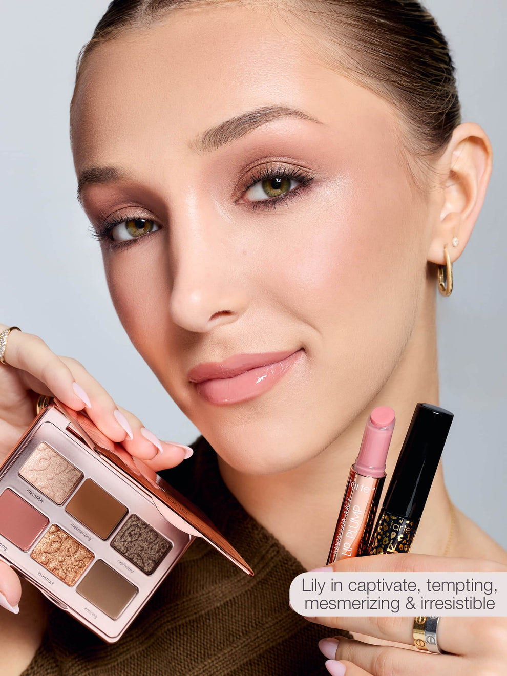 A person holds a Tarte Cosmetics eyeshadow palette with various shades, a lip crayon, and a mascara in a well-lit setting. Text reads: Lily in captivate, tempting, mesmerizing & irresistible.