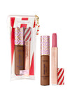 A set of three Tarte Cosmetics products includes two tubes and a wand applicator, displayed with a decorative bag. The tubes have geometric and striped patterns, suggesting a festive theme.