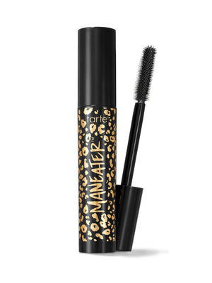 O tubo de rímel está na vertical, com o aplicador retirado e colocado ao seu lado, num ângulo; o tubo, gold em preto e gold , tem a inscrição «tarte™ MANEATER™» num fundo branco.