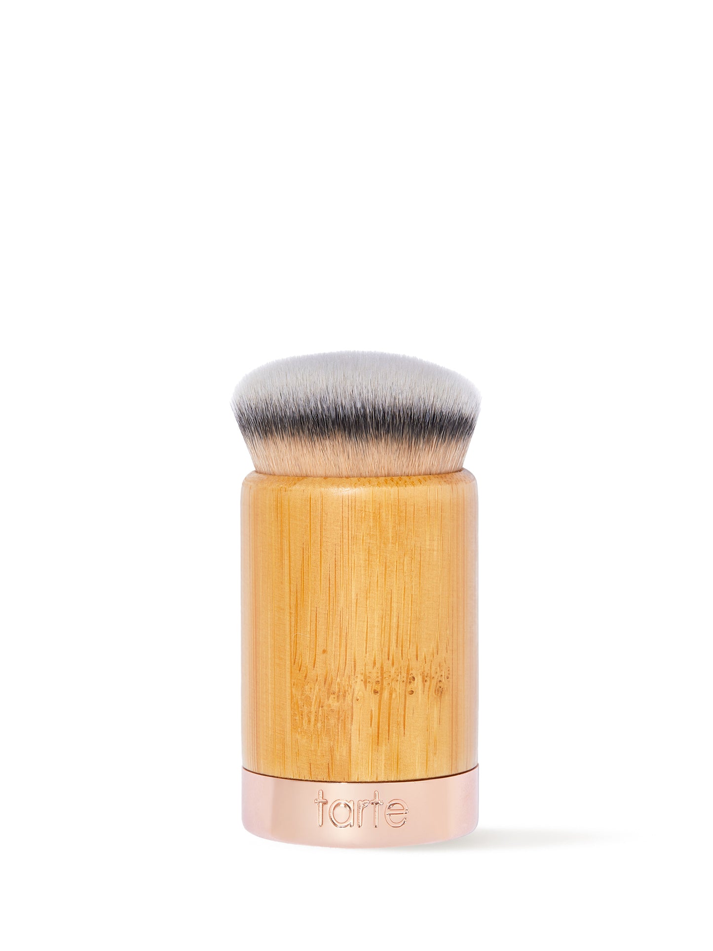 A dense, round makeup brush with soft bristles sits upright. The handle is wooden with a metal base etched with tarte, set against a plain white background.