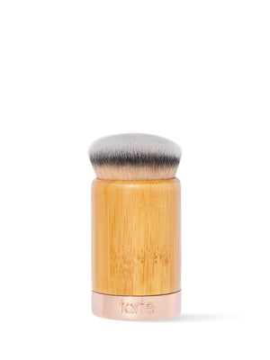 Ein dichter, runder Make-up-Pinsel mit weichen Borsten steht aufrecht da. Der Griff ist aus Holz und hat einen Metallsockel, auf dem „tarte“ eingraviert ist; er hebt sich von einem schlichten weißen Hintergrund ab.