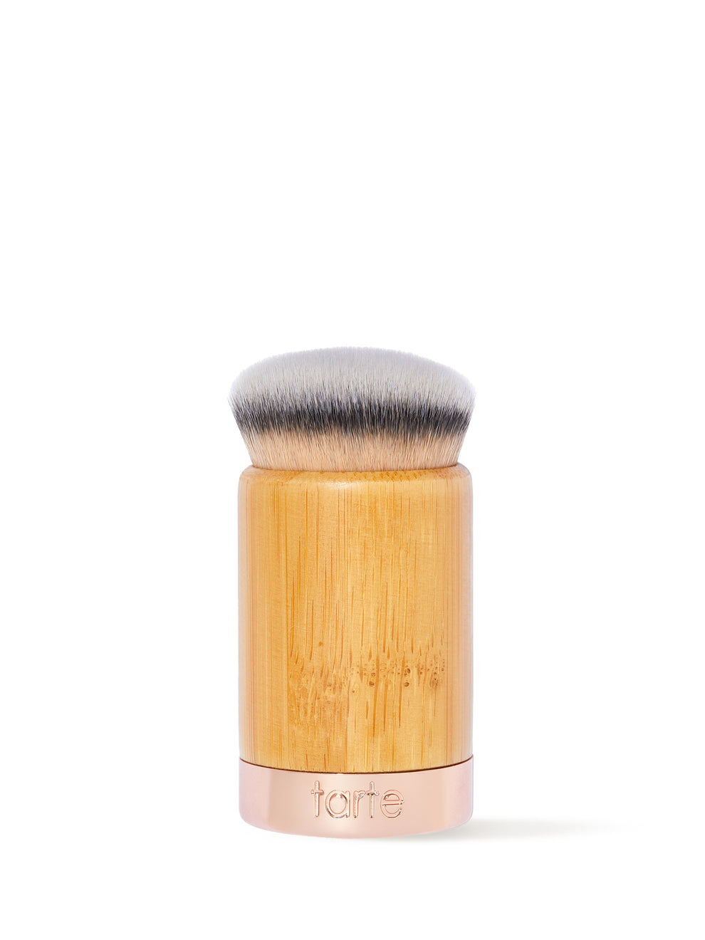 A dense, round makeup brush with soft bristles sits upright. The handle is wooden with a metal base etched with tarte, set against a plain white background.