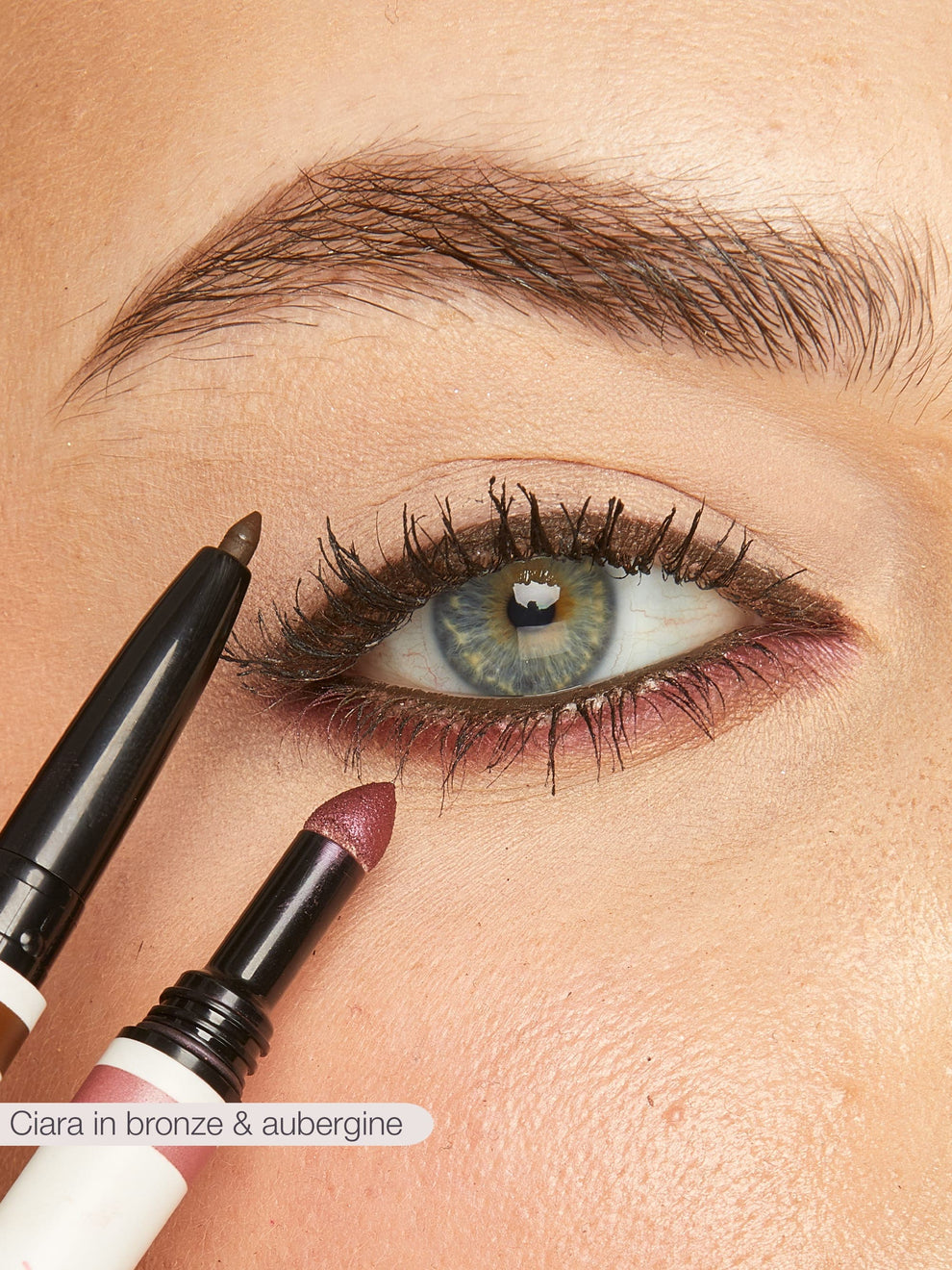 Close-up of a person applying eyeliner with a pencil and lipstick with a brush.