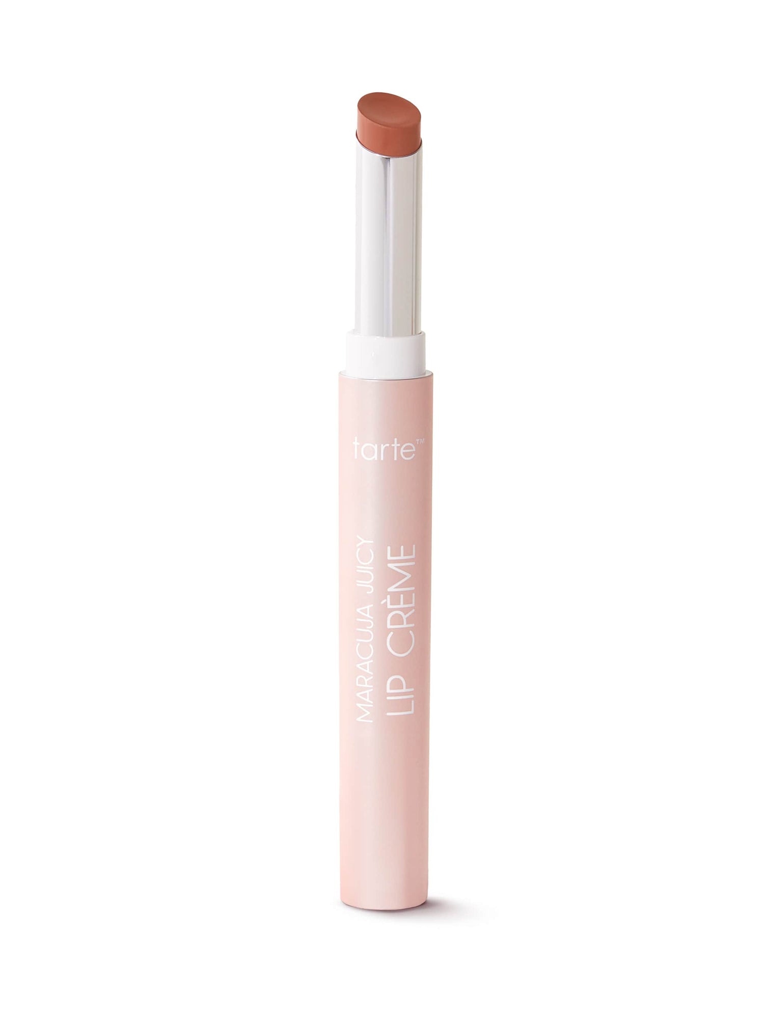 A slim, cylindrical lipstick is extended upward, displaying a light brown shade; it stands vertically against a white backdrop. The packaging is light pink with Tarte printed on it.