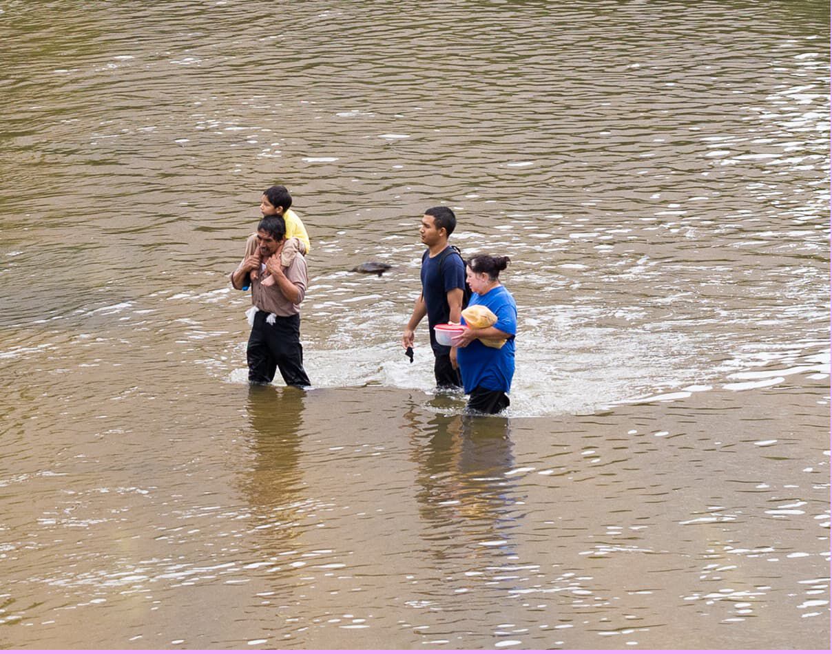 three adults and one kid walking through flooded street affected by a natural disaster